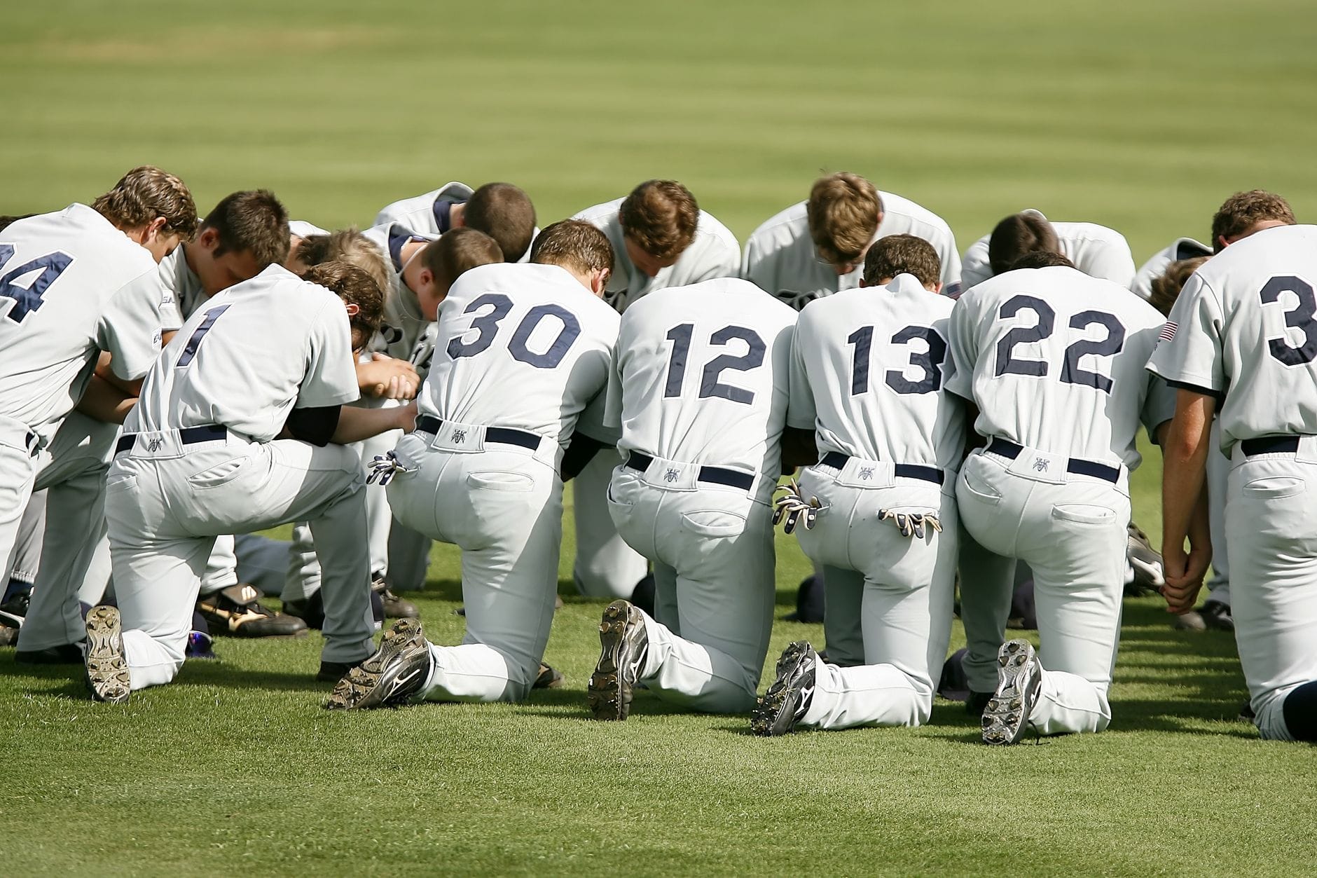 Grupa baseballistów w strojach klęczących razem na boisku